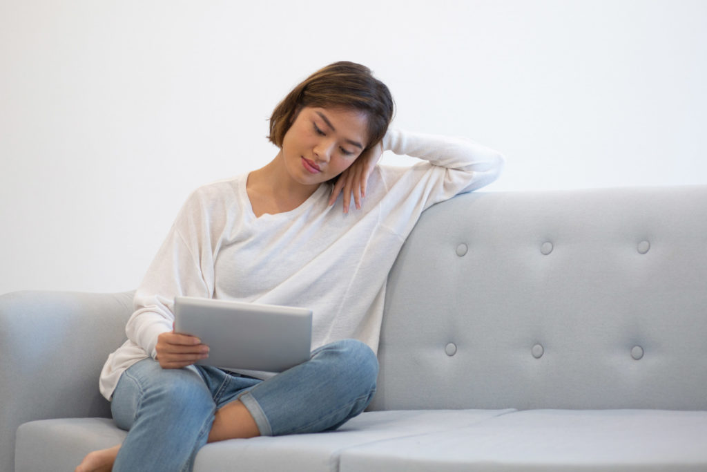 woman sitting on the couch reading on a tablet